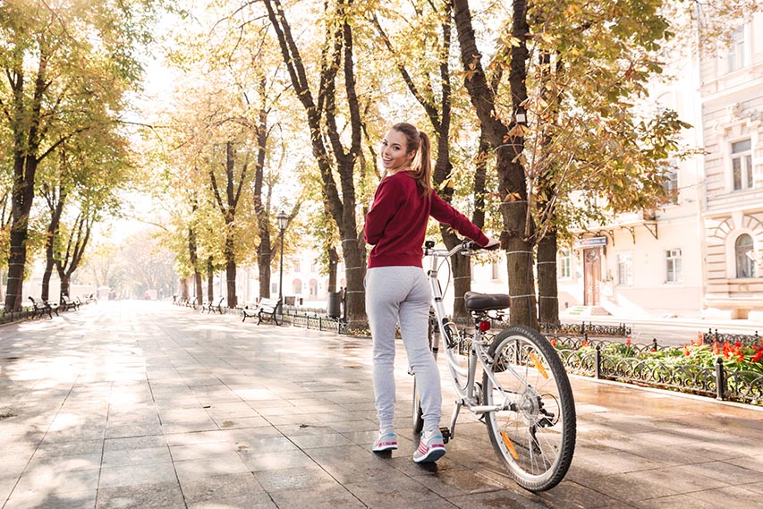 Joyful Lady Dressed In Sweater Walking With Her Bicycle Outdoors