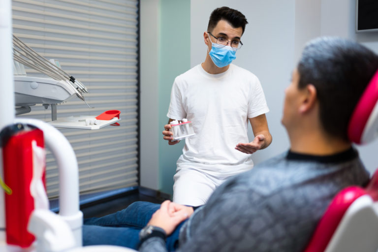 牙周病初期症狀有哪些?出現這些症狀要小心 1 Dental Surgeon With Dental Crown In Hands Model Talks To Patient About Prosthetics Man At The Dentist S Appointment